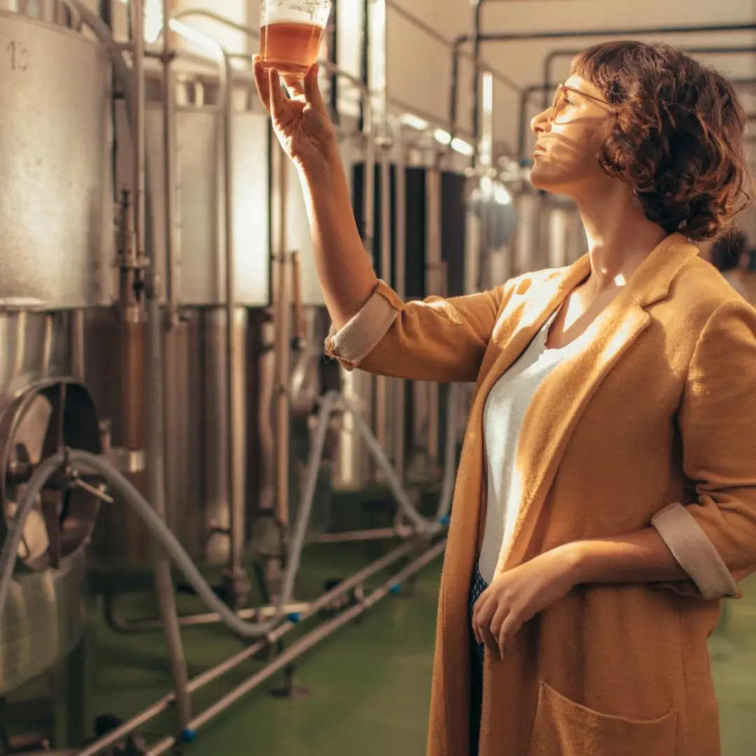 Frau, die das frische Bier prüft. Sie steht in einer Brauerei.